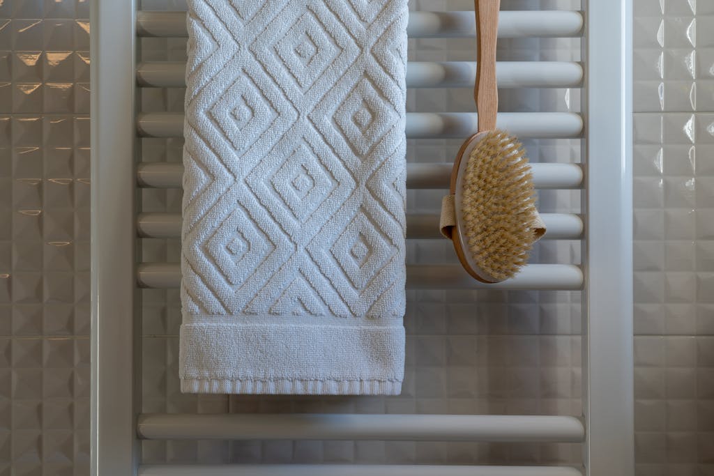 Elegant white towel with geometric pattern on bathroom towel rail, paired with a natural bristle brush.